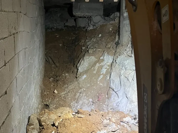 חפירת מרתף מתחת לבית קיים: כף מיני מחפרון בחלל צר בין קיר בלוקים לסלע חשוף