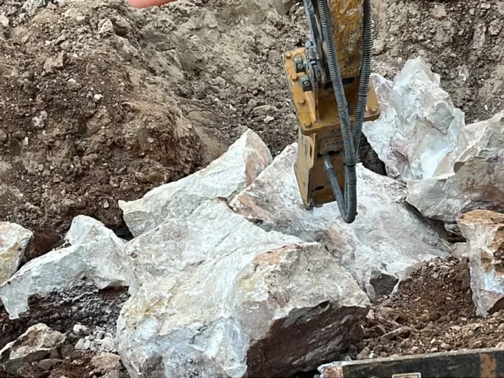פטיש הידראולי על מיני מחפרון שובר גושי סלע גיר לבנים בתוך בור חפירה