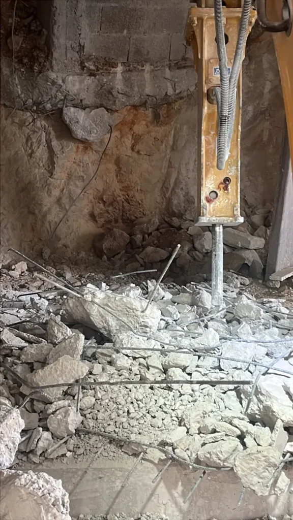 פטיש הידראולי חוצב סלע גיר ושובר בטון מזוין בבסיס קיר של מבנה