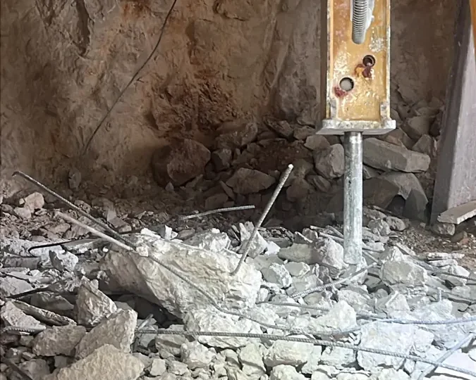 פטיש הידראולי חוצב סלע גיר ושובר בטון מזוין בבסיס קיר של מבנה