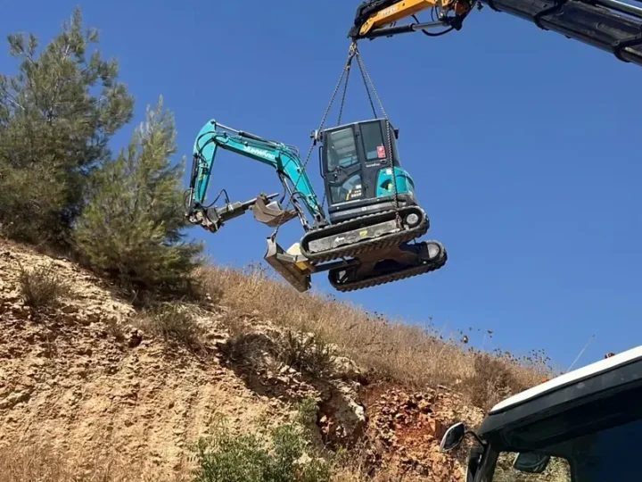 מנוף מרים מיני מחפרון זחלי באוויר מעל מדרון סלעי, להעברה לשטח שקשה להגיע אליו