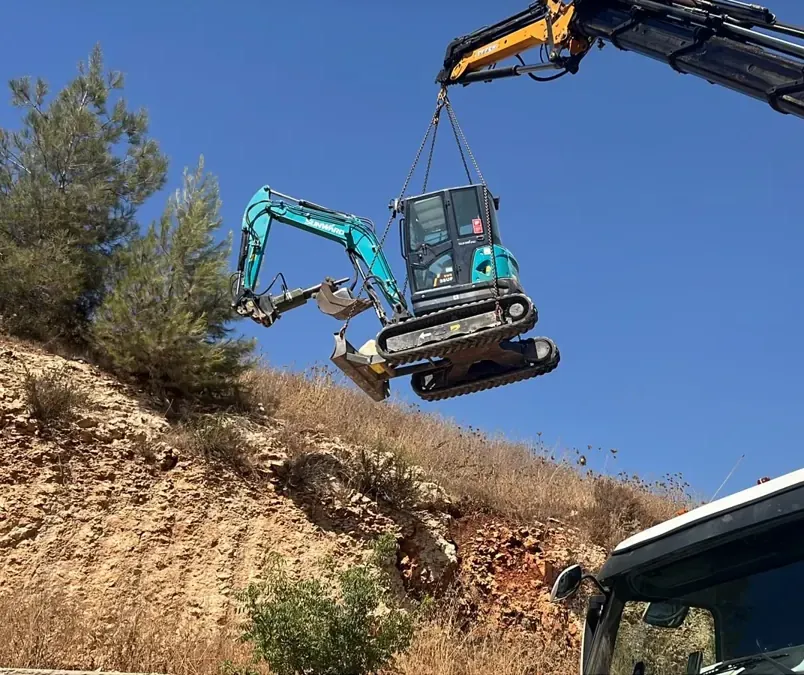 מנוף מרים מיני מחפרון זחלי באוויר מעל מדרון סלעי, להעברה לשטח שקשה להגיע אליו