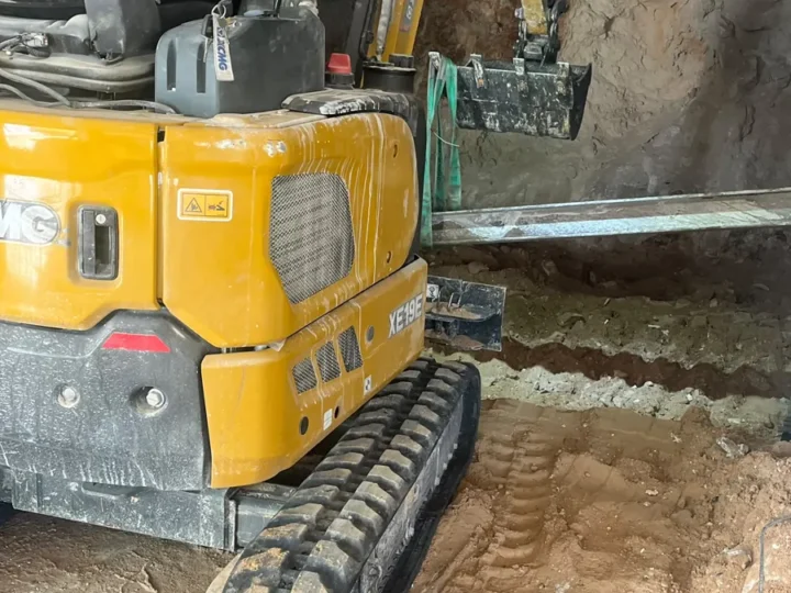 מיני מחפרון חופר מרתף בתוך מבנה קיים מתחת לתקרה, ליד קורת פלדה תומכת