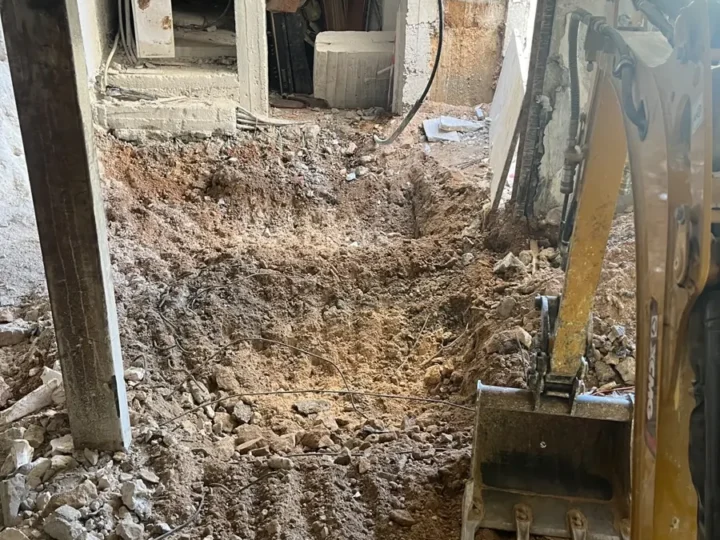 מיני מחפרון מנמיך רצפה בתוך מבנה קיים, בין עמודי פלדה ובטון