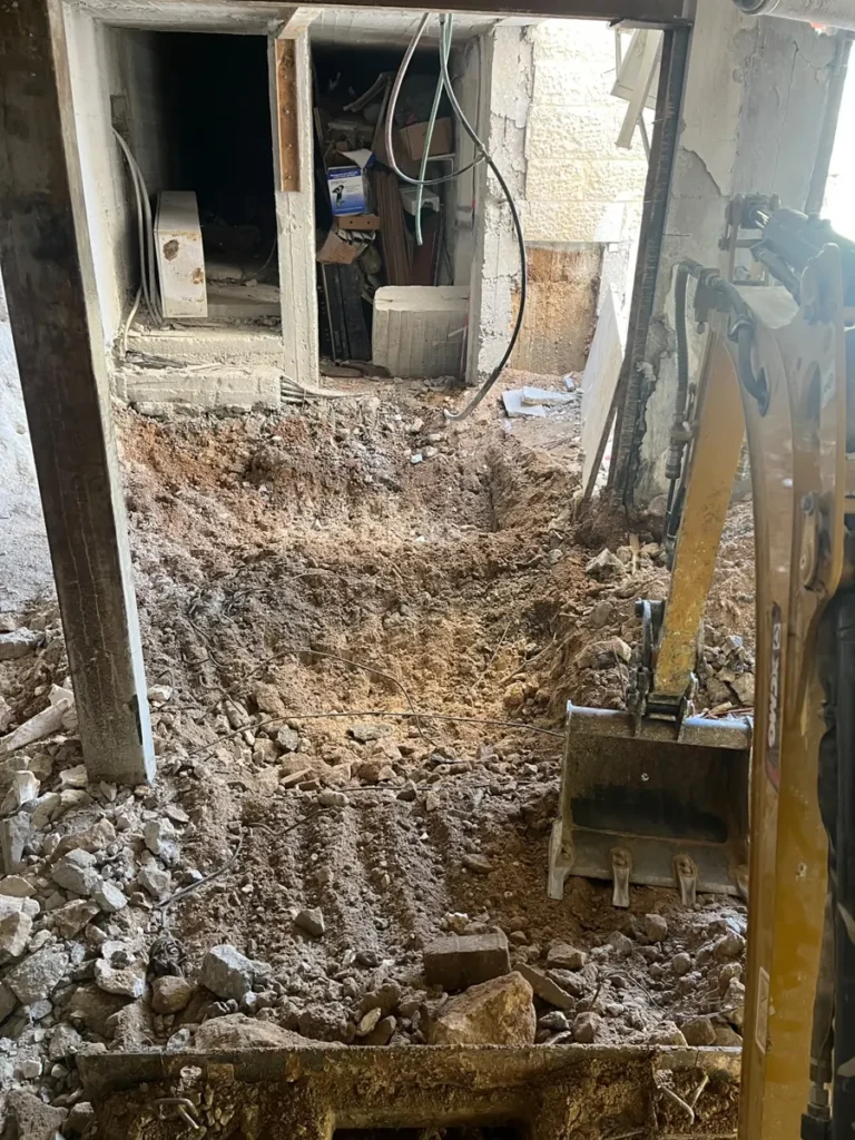 מיני מחפרון מנמיך רצפה בתוך מבנה קיים, בין עמודי פלדה ובטון