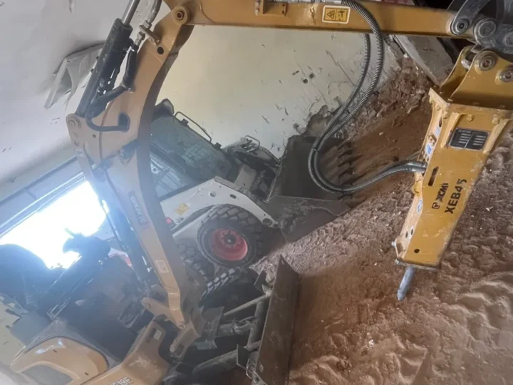 מיני מחפרון עם פטיש הידראולי ובובקט עובדים יחד בתוך חדר בקומת קרקע
