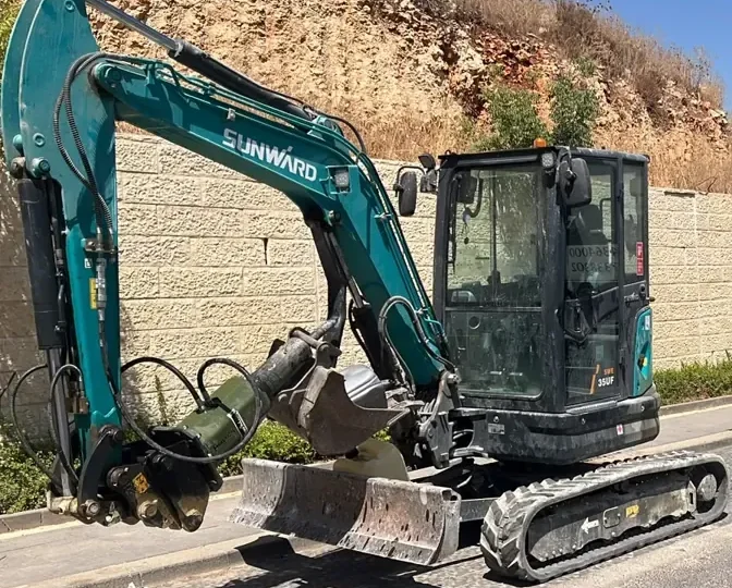 מיני מחפרון עם פטיש הידראולי ברחוב ליד קיר אבן, רגע לפני הורדה מהמשאית
