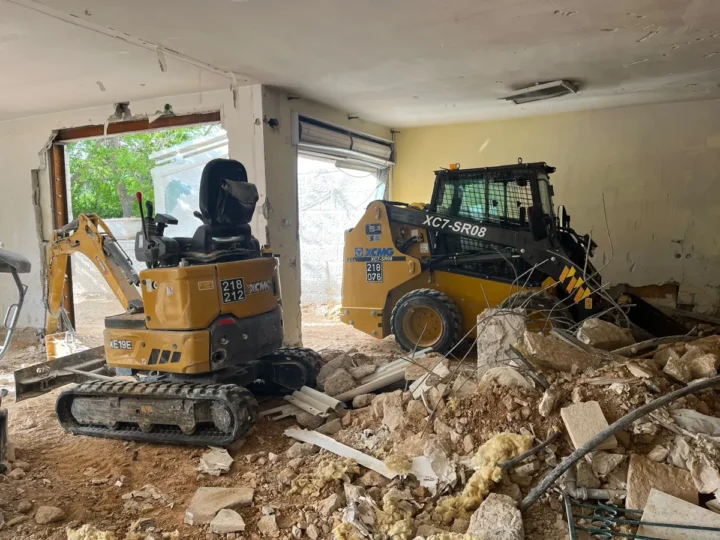 מיני מחפרון ובובקט בתוך חדר בבית קיים, בין פסולת בניין, ברזלים ואבנים לפני פינוי